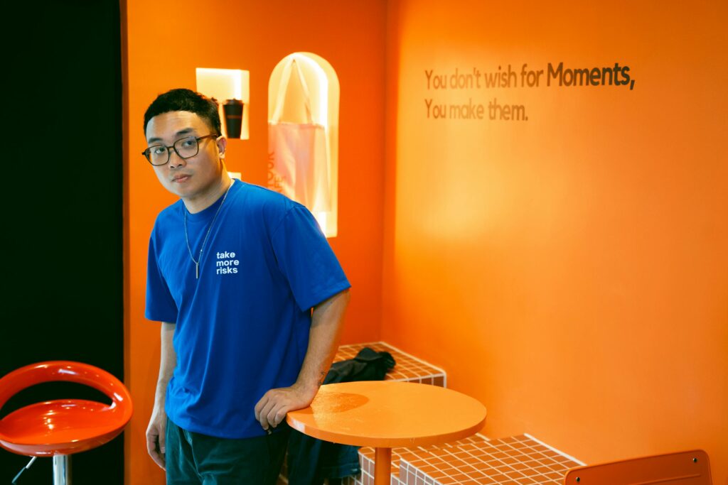 Man in a blue shirt posing in an orange themed room with motivational text on the wall.