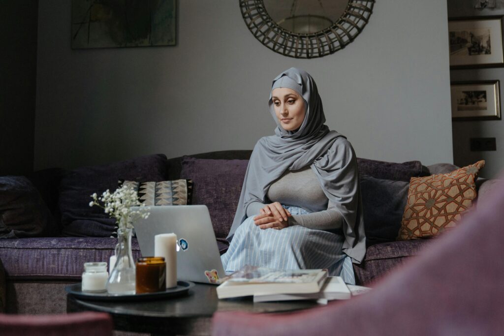 Middle Eastern woman sitting on a sofa working on a laptop in a living room setting.